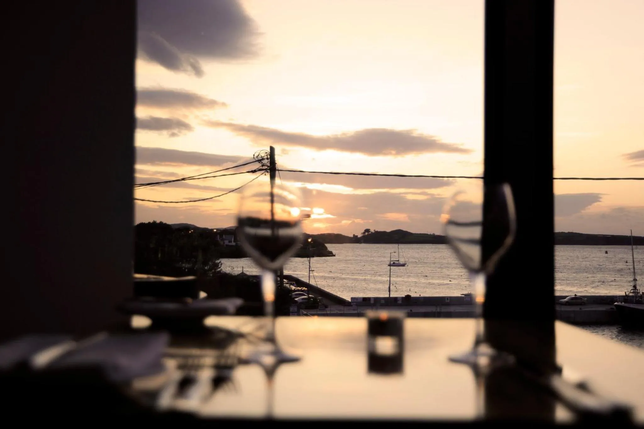 Deux verres de vin sur une table face à la mer au coucher du soleil.