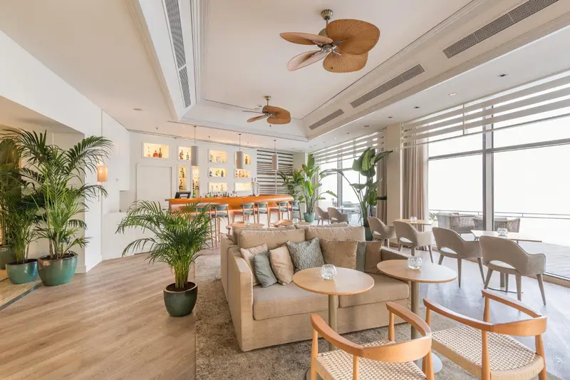 Espace de détente intérieur avec canapés et tables basses, éclairé par de grandes baies vitrées.
