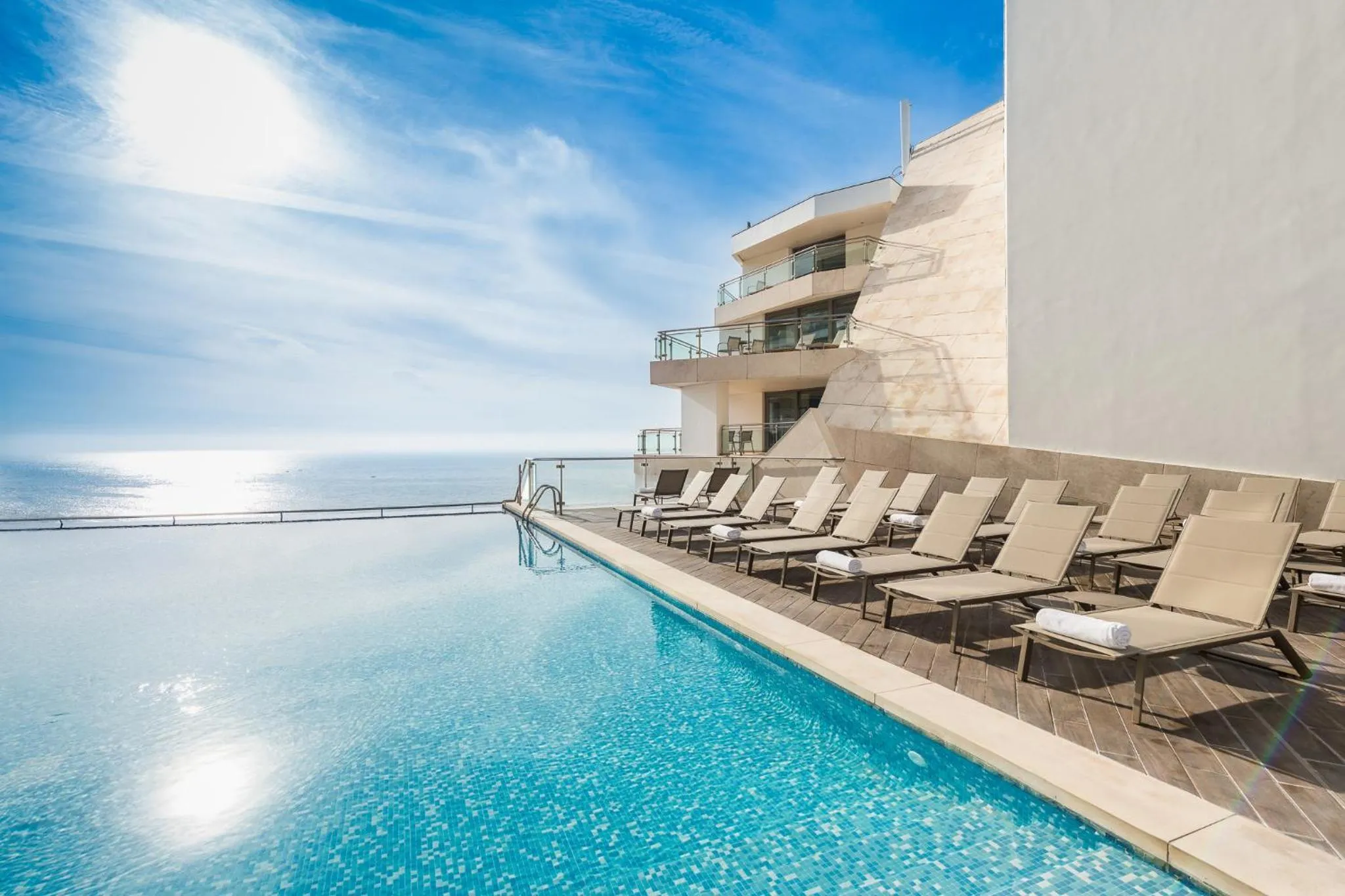 Transats alignés au bord d'une piscine à débordement avec vue sur la mer.
