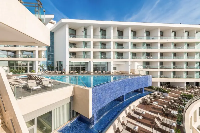 Bâtiment blanc moderne avec piscine à débordement et terrasses ensoleillées.