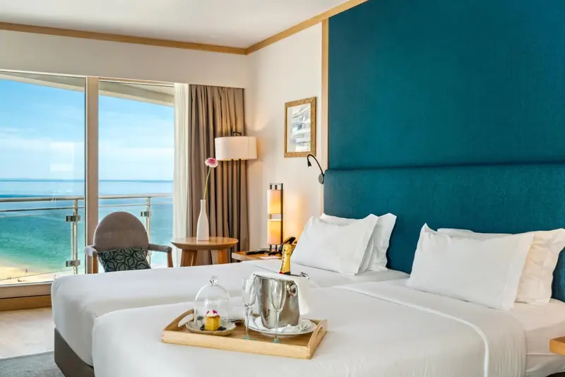 Chambre lumineuse avec un lit blanc et une vue sur la mer.