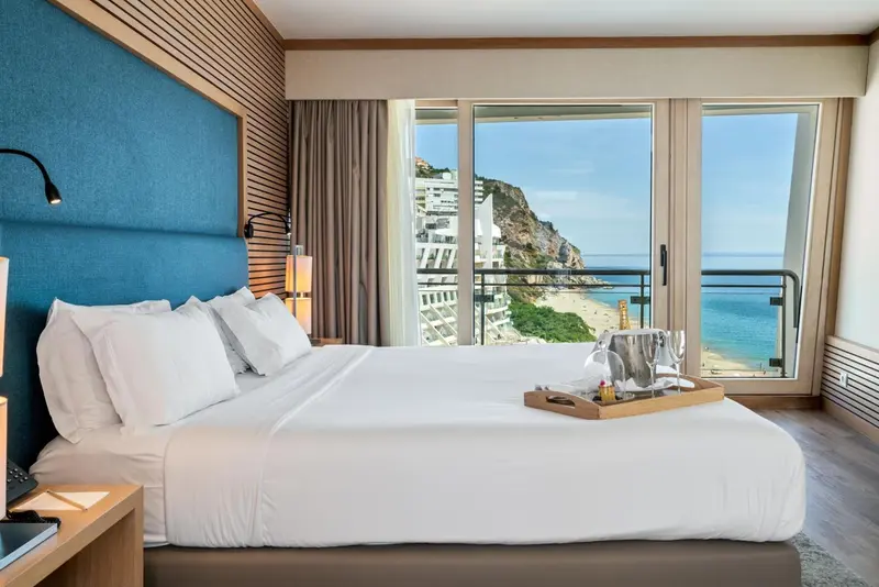 Une chambre lumineuse avec un grand lit face à une baie vitrée donnant sur la mer.