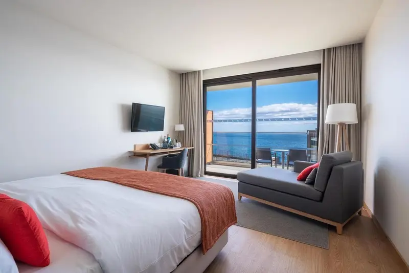 Une chambre lumineuse avec un lit et un coin salon donnant sur la mer.