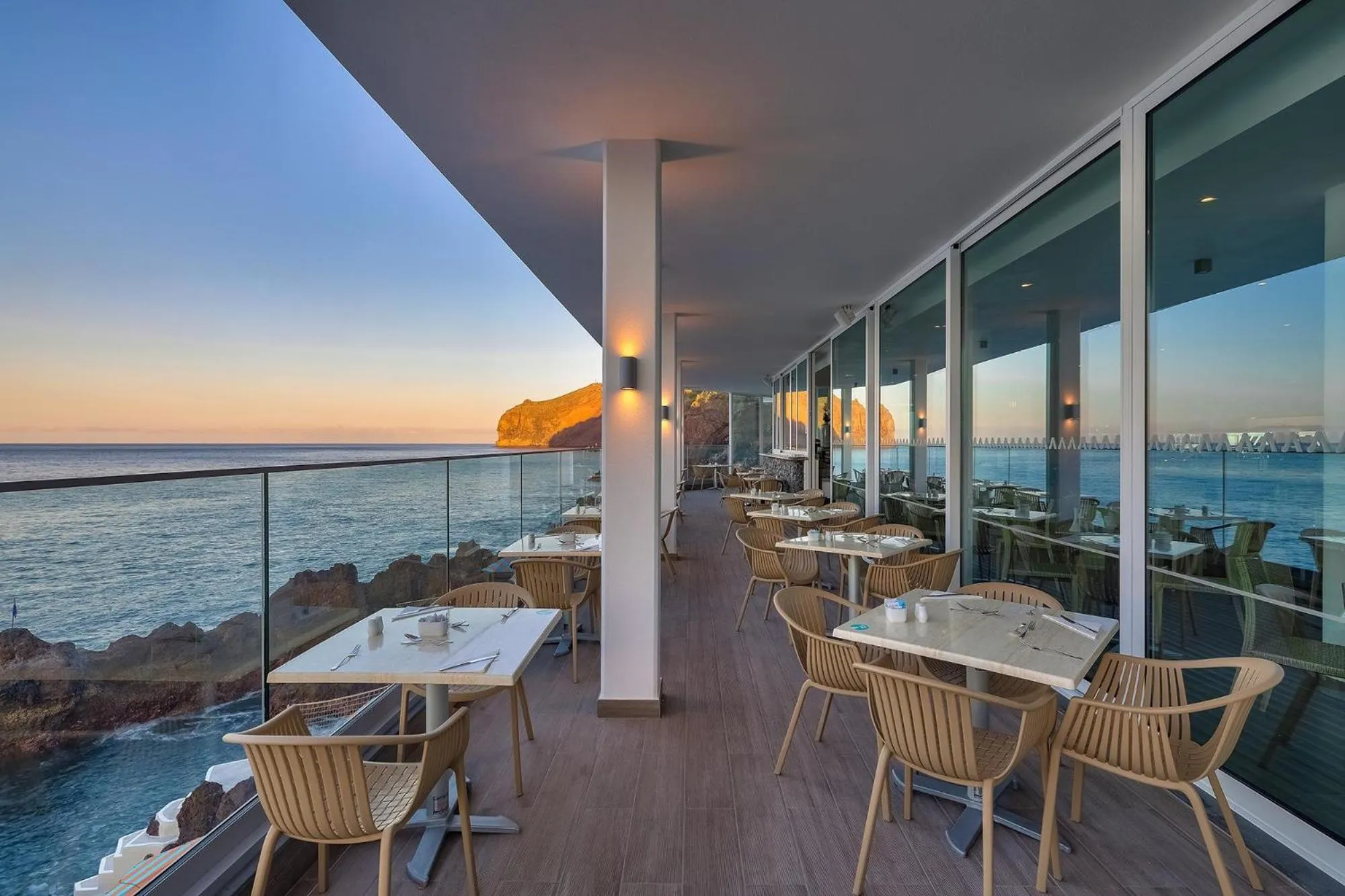 Terrasse avec tables et chaises donnant sur la mer au coucher du soleil.