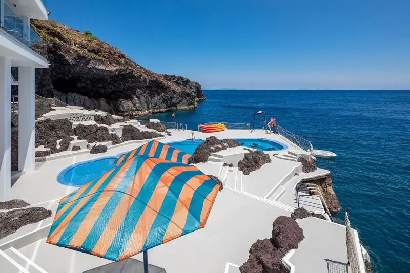 Terrasse avec parasols rayés donnant sur une piscine et la mer.
