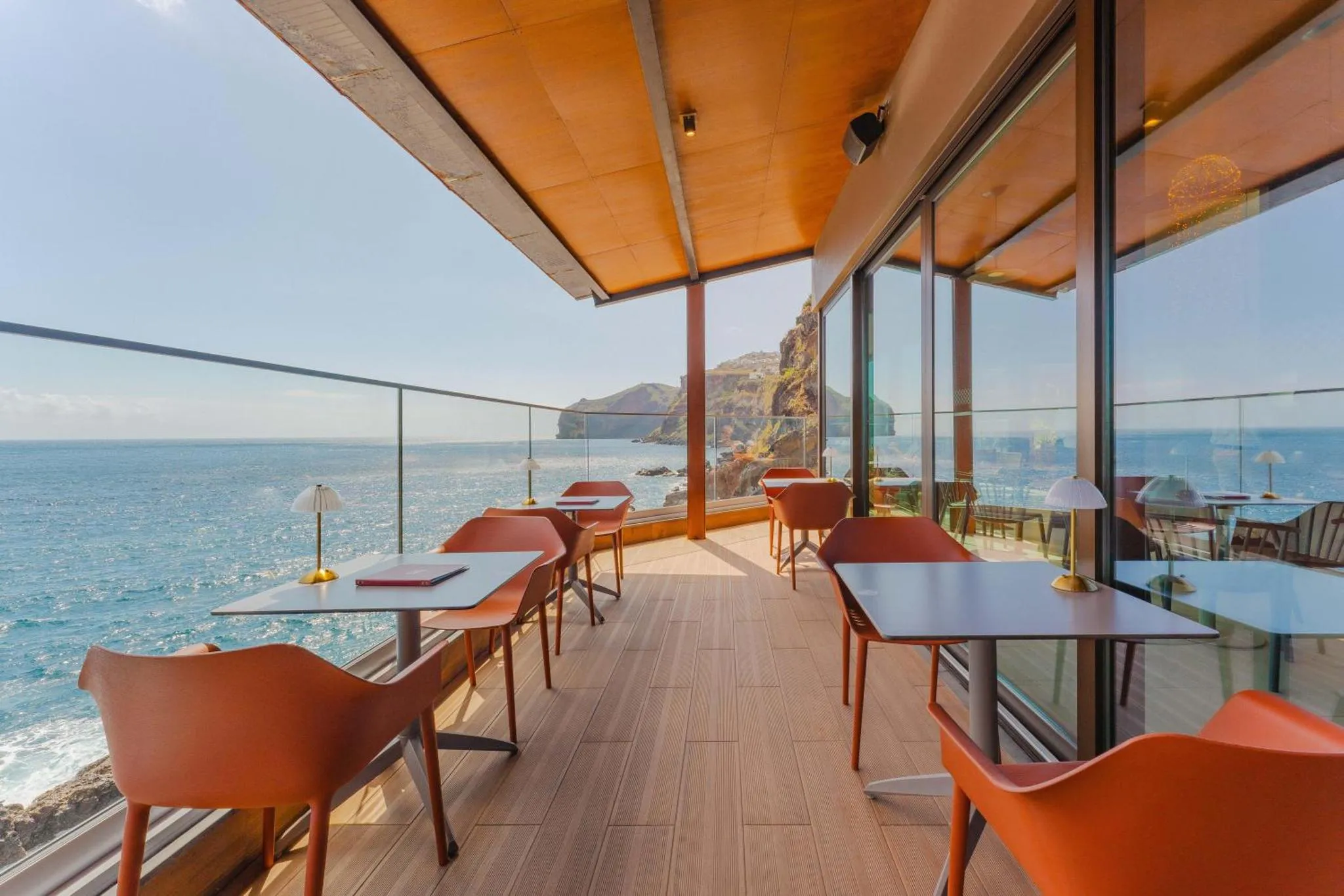 Terrasse avec tables et chaises donnant sur l'océan et des formations rocheuses.