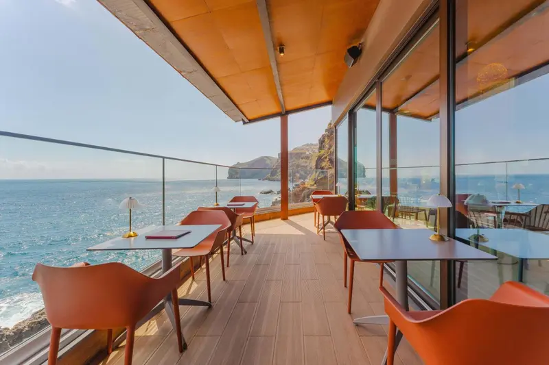 Terrasse avec tables et chaises donnant sur l'océan et des formations rocheuses.