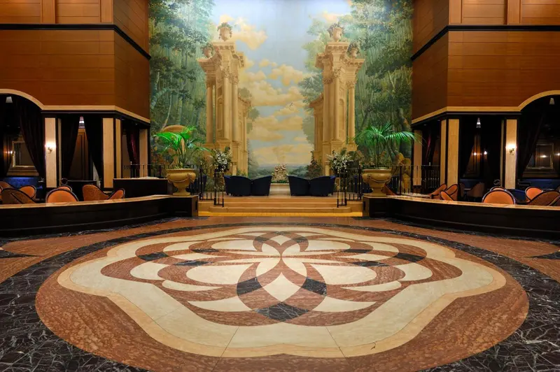 Vaste hall d'entrée avec sol en mosaïque et fresque murale représentant une allée de colonnes.
