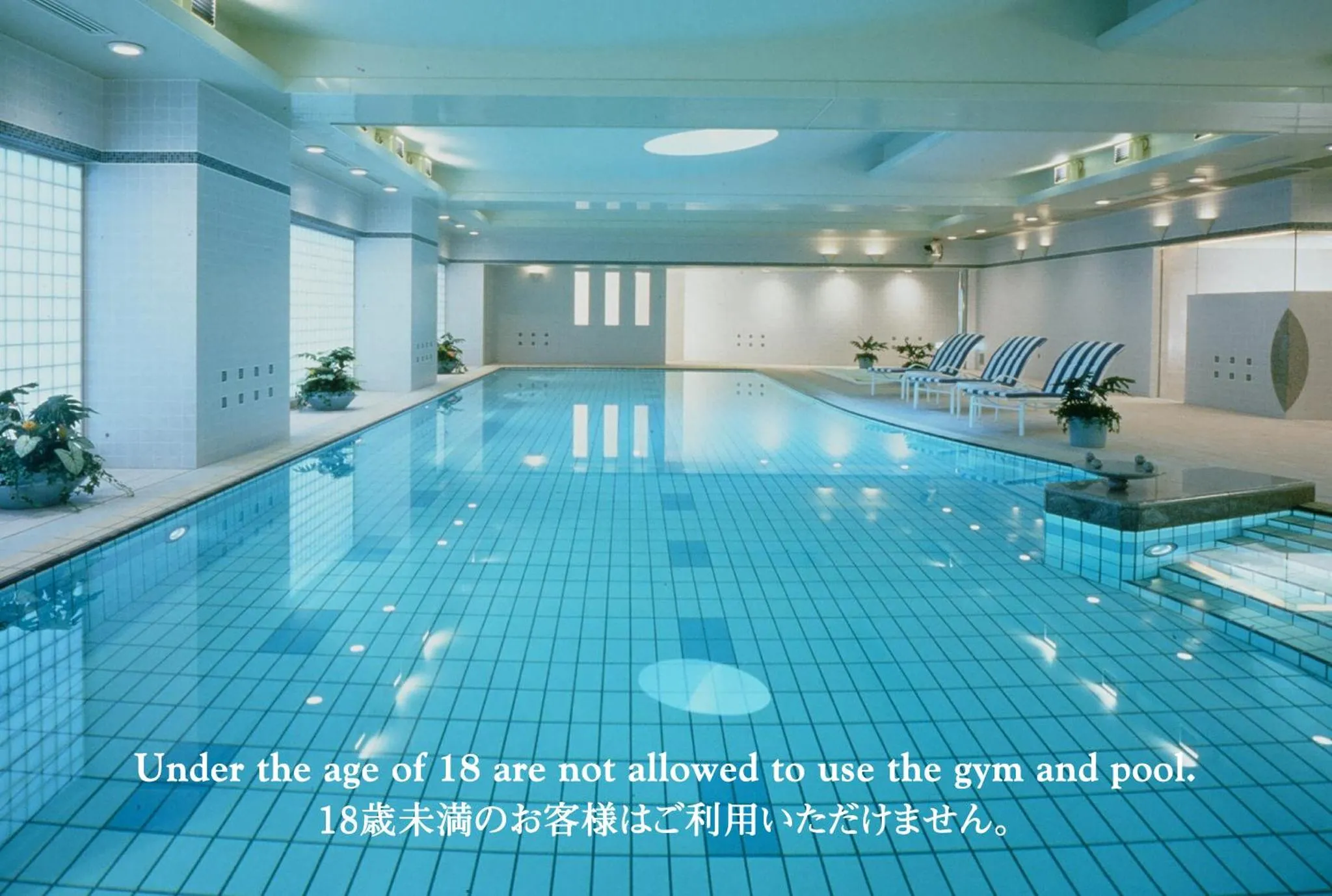 Une piscine intérieure rectangulaire avec des transats bleus alignés sur le bord.