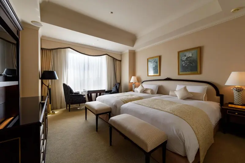 Chambre d'hôtel avec deux lits simples et une fenêtre drapée.