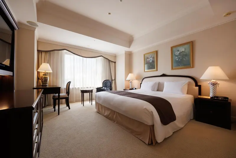 Une chambre lumineuse avec un grand lit et un bureau près de la fenêtre.