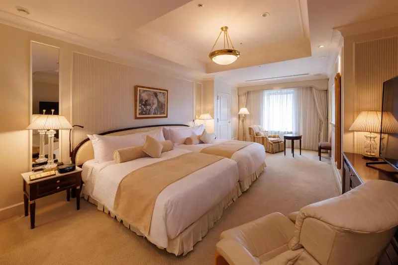 Chambre lumineuse avec deux lits et fauteuils.