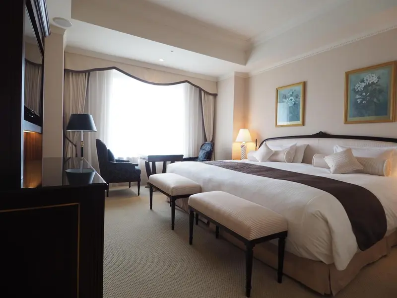Une chambre lumineuse avec un grand lit et un coin salon près de la fenêtre.