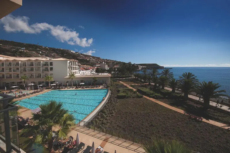 Vue aérienne d'un complexe hôtelier avec piscine et végétation luxuriante face à la mer.