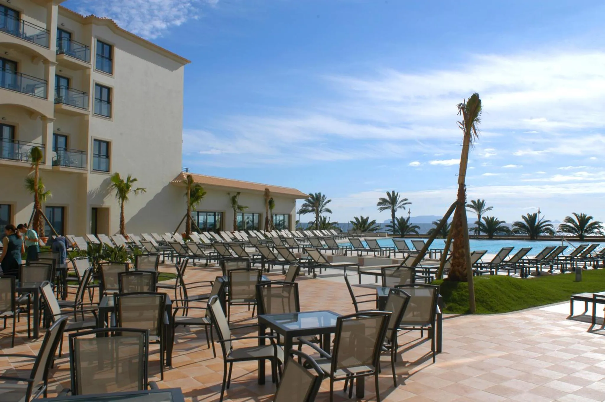 Terrasse ensoleillée avec transats et tables basses près d'une piscine.