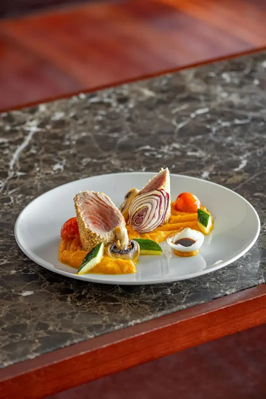 Assiette de poisson agrémentée de légumes et de sauce.