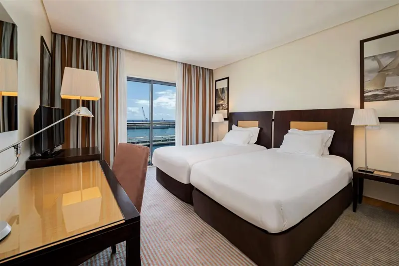 Chambre d'hôtel lumineuse avec deux lits simples et vue sur le port.