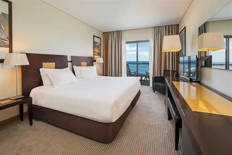 Chambre lumineuse avec un grand lit et une vue sur la mer.