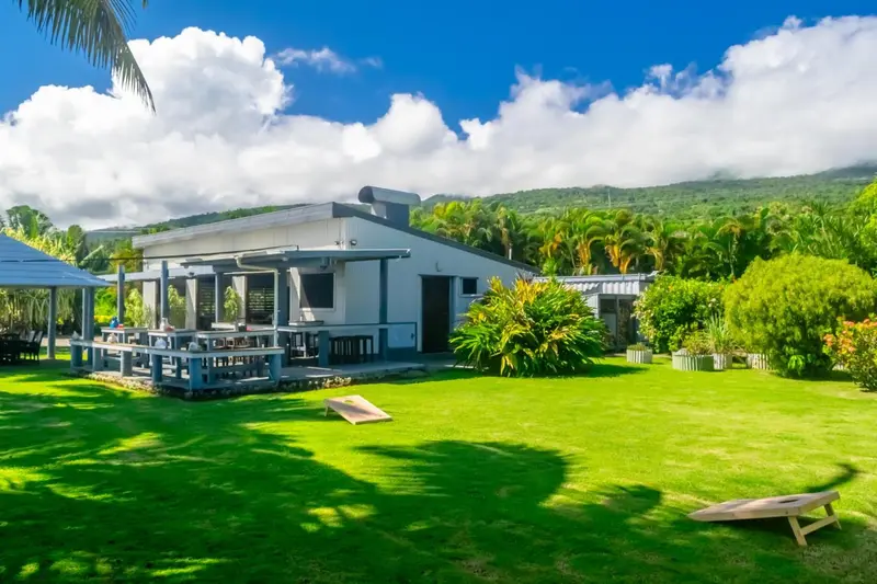 Bâtiment moderne avec une terrasse ombragée donnant sur une pelouse verdoyante et des collines.
