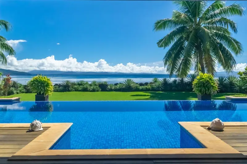 Une piscine bleue reflète le ciel et la végétation tropicale.