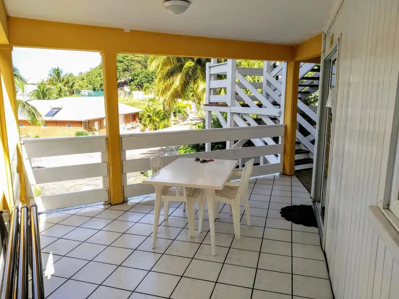 Une terrasse carrelée avec une table et des chaises blanches offre une vue sur la végétation.