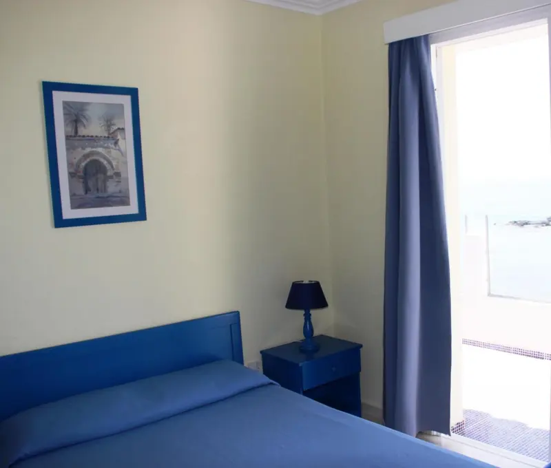 Une chambre lumineuse avec un lit bleu et une vue sur la mer.