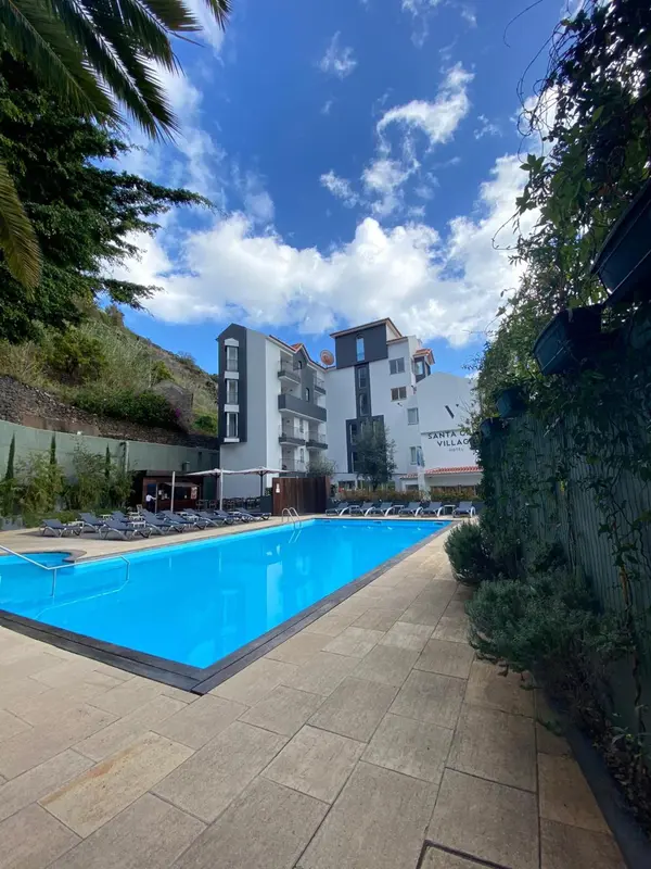 Une piscine rectangulaire turquoise est bordée de chaises longues devant un bâtiment blanc à plusieurs étages.