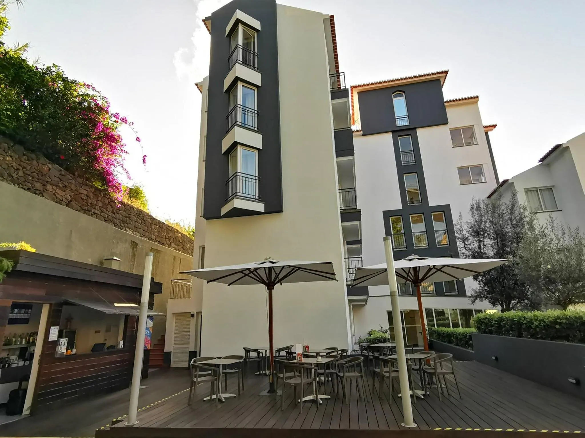 Terrasse ombragée avec tables et chaises devant un bâtiment moderne.