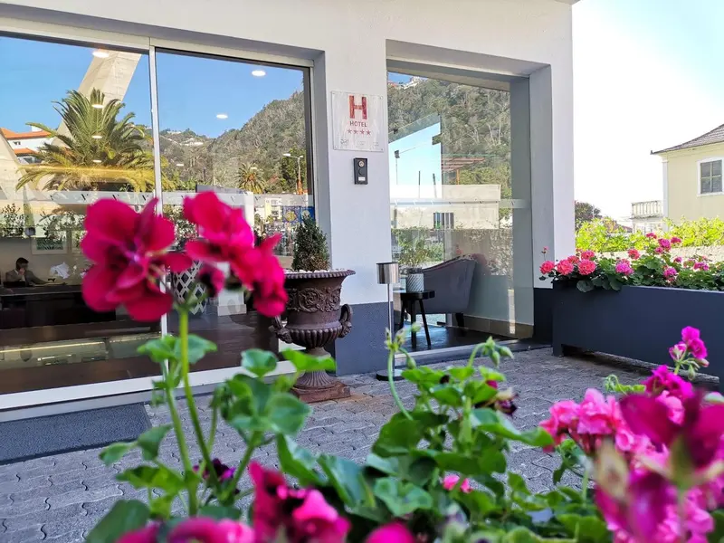 Façade d'un hôtel avec des fleurs en premier plan et une vue sur la mer.