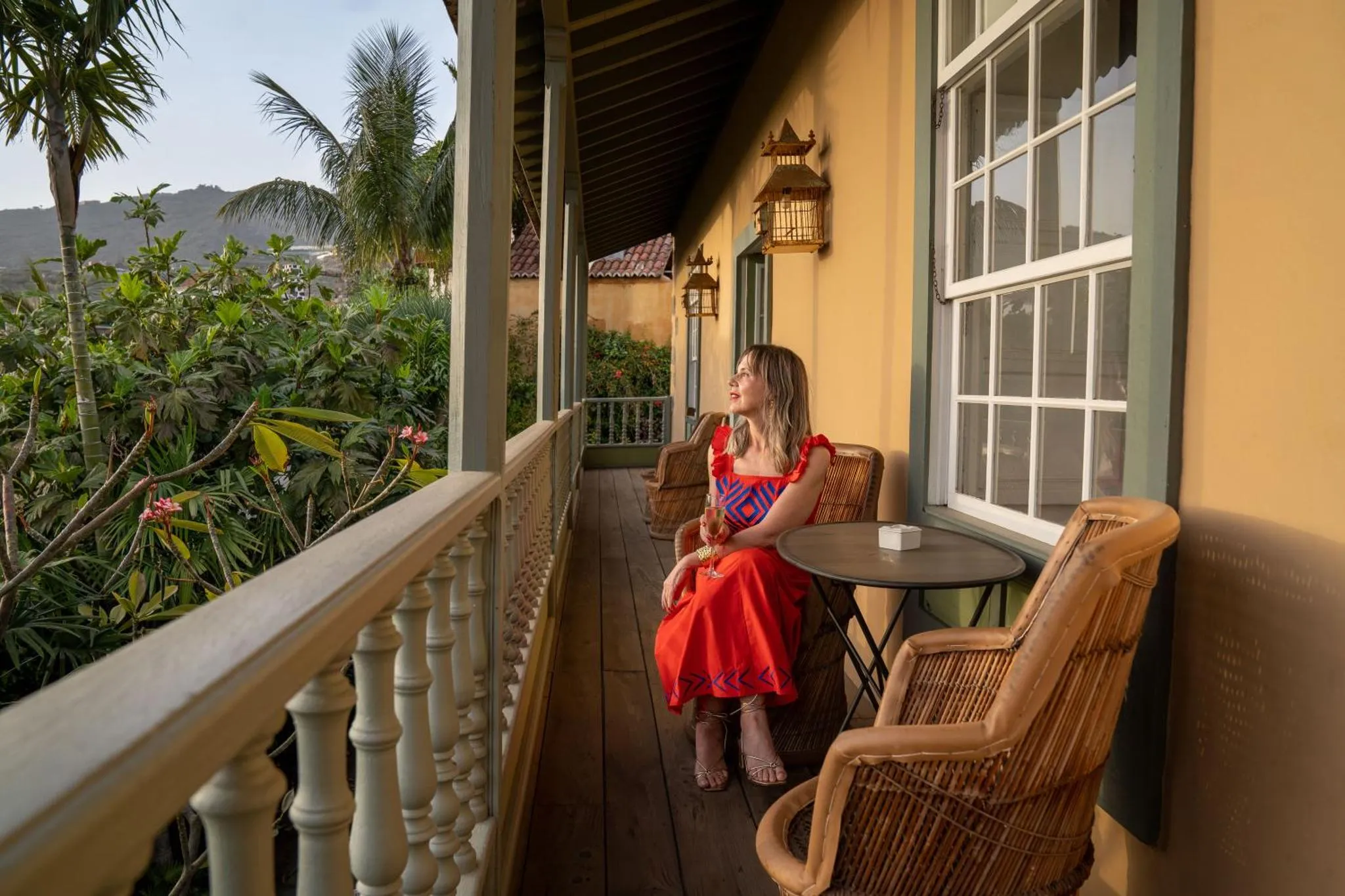 Une femme assise sur une terrasse ensoleillée avec vue sur la végétation.
