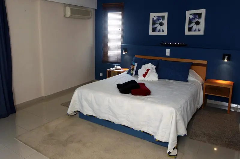 Une chambre lumineuse avec un grand lit recouvert d'une courtepointe blanche et de coussins bleus.
