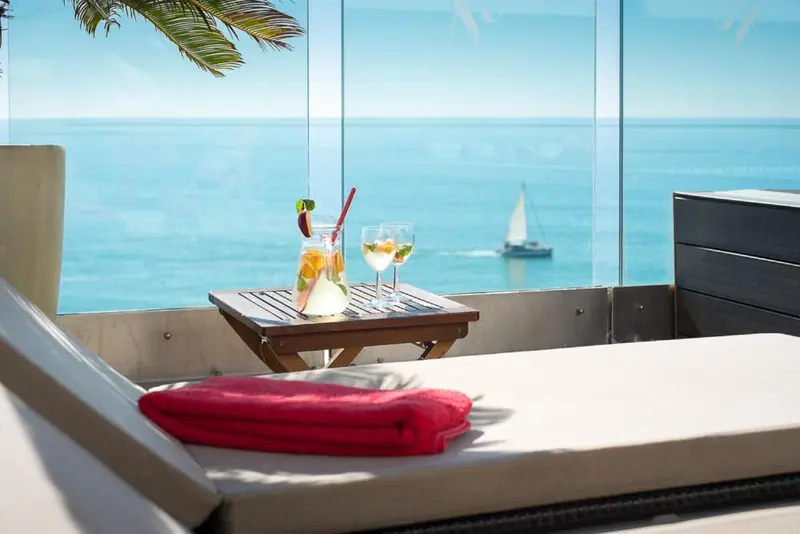Deux cocktails colorés sur une table basse, avec vue sur la mer depuis une terrasse.