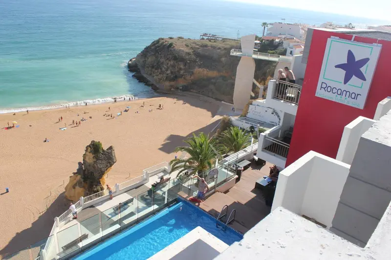 Vue aérienne d'une plage de sable fin bordée de falaises et d'un hôtel avec piscine.