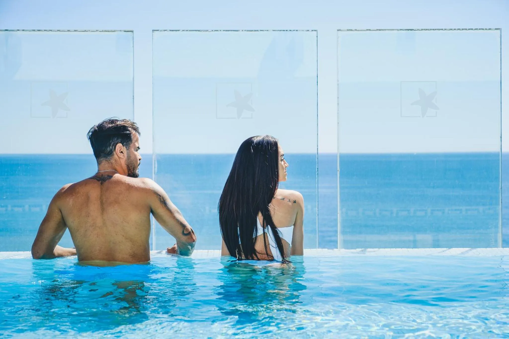 Un couple se tient au bord d'une piscine à débordement face à la mer.