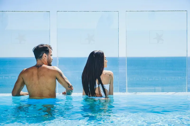 Un couple se tient au bord d'une piscine à débordement face à la mer.