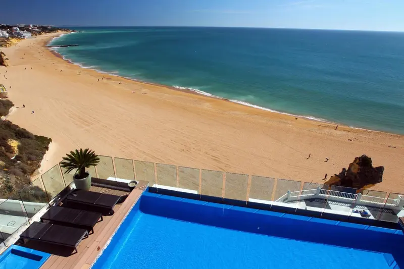 Vue aérienne d'une plage de sable fin bordée d'une eau turquoise et d'une piscine à débordement.