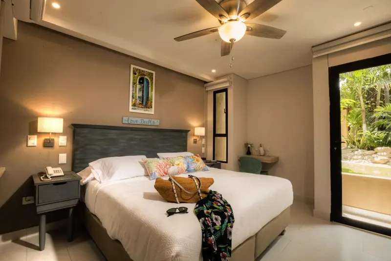 Une chambre lumineuse avec un grand lit recouvert d'une courtepointe blanche et de coussins colorés.