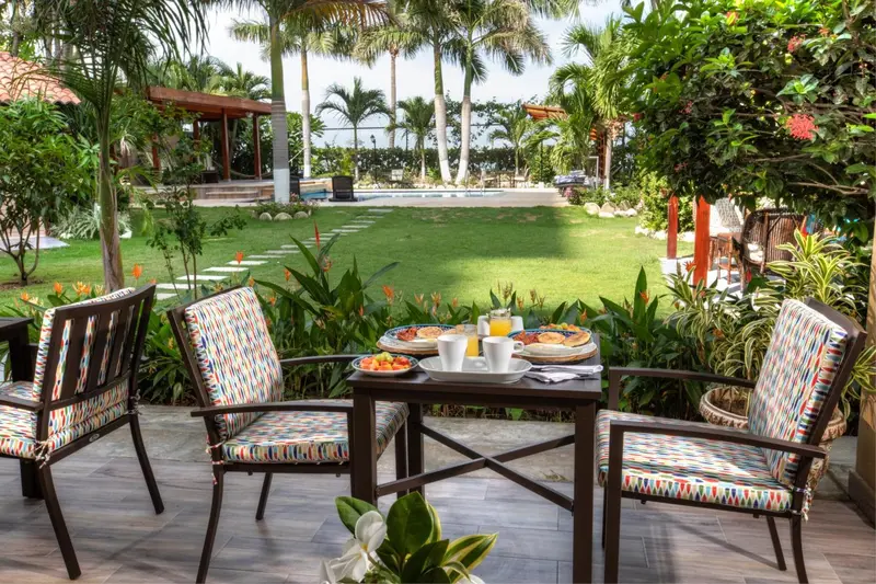 Une table de petit-déjeuner est mise en scène sur une terrasse verdoyante.