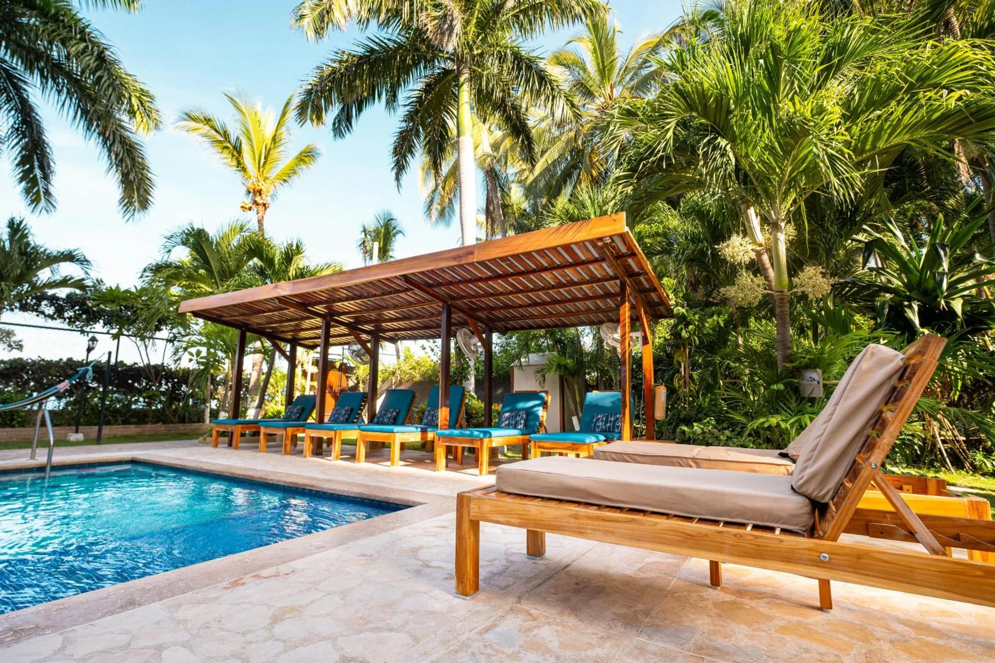 Transats en bois disposés autour d'une piscine bordée de végétation tropicale.