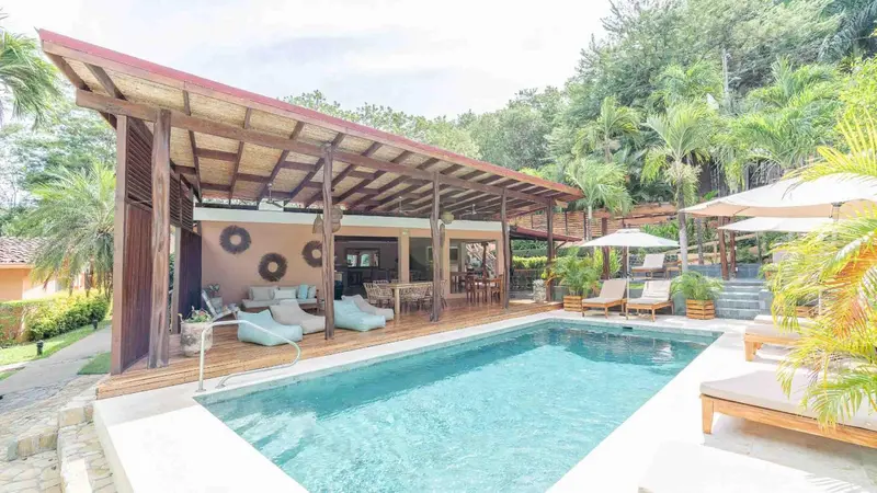 Une piscine turquoise bordée de chaises longues et de végétation luxuriante.