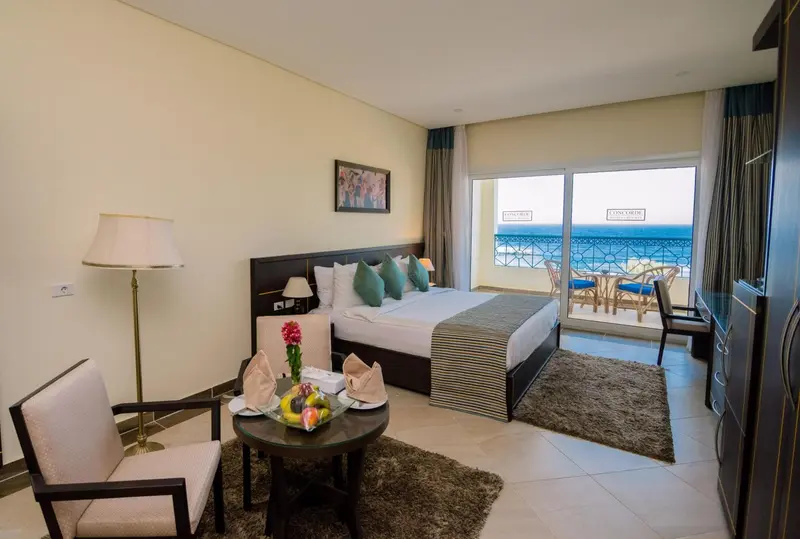 Chambre lumineuse avec un lit double et un coin salon donnant sur la mer.