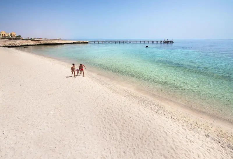 Plage de sable blanc bordée d'une eau turquoise et d'une falaise rocheuse.