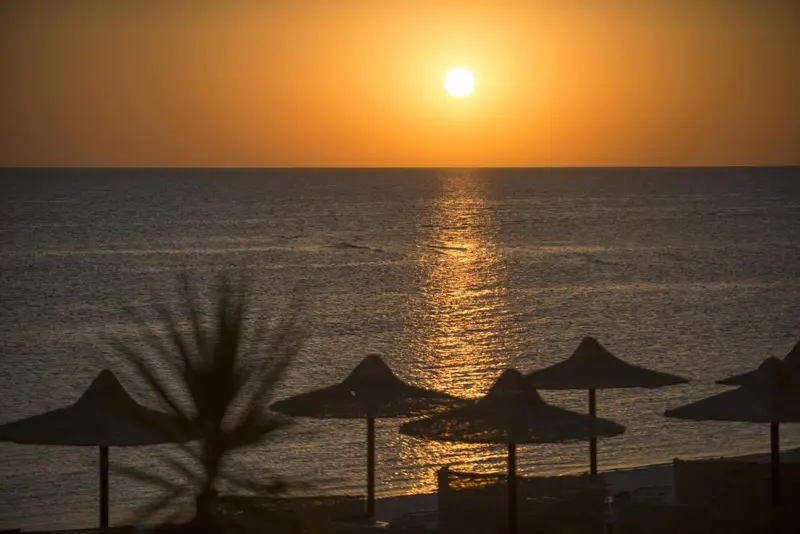 Le soleil se couche sur la mer, illuminant les parasols sur la plage.