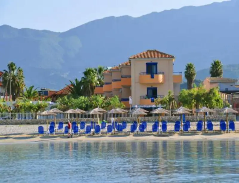 Bâtiment blanc et ocre avec des transats bleus sur une plage ensoleillée.