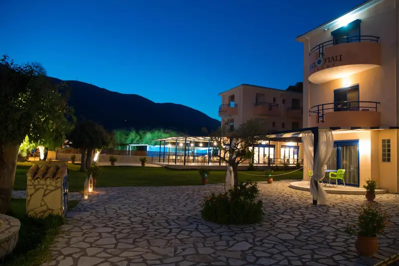 Bâtiment blanc illuminé au crépuscule avec jardin verdoyant et mobilier d'extérieur.