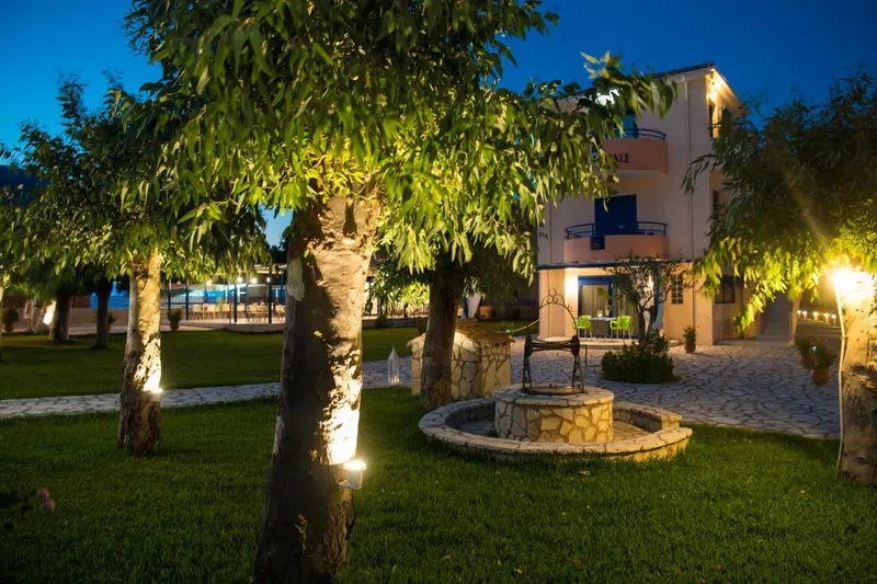 Bâtiment éclairé au crépuscule avec un jardin verdoyant et une fontaine en pierre.