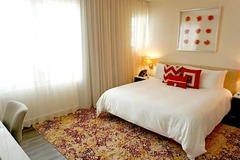 Une chambre lumineuse avec un grand lit recouvert d'une couette blanche et de coussins colorés.