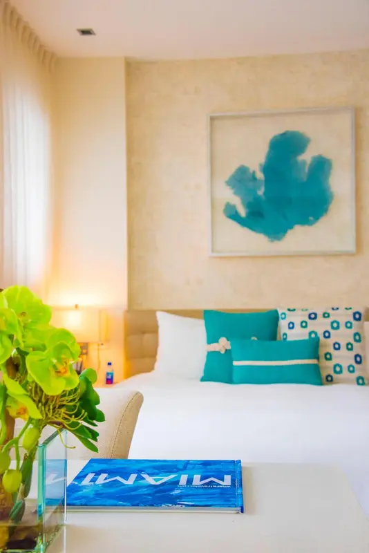 Une chambre lumineuse avec un lit recouvert d'une courtepointe blanche et de coussins turquoise.