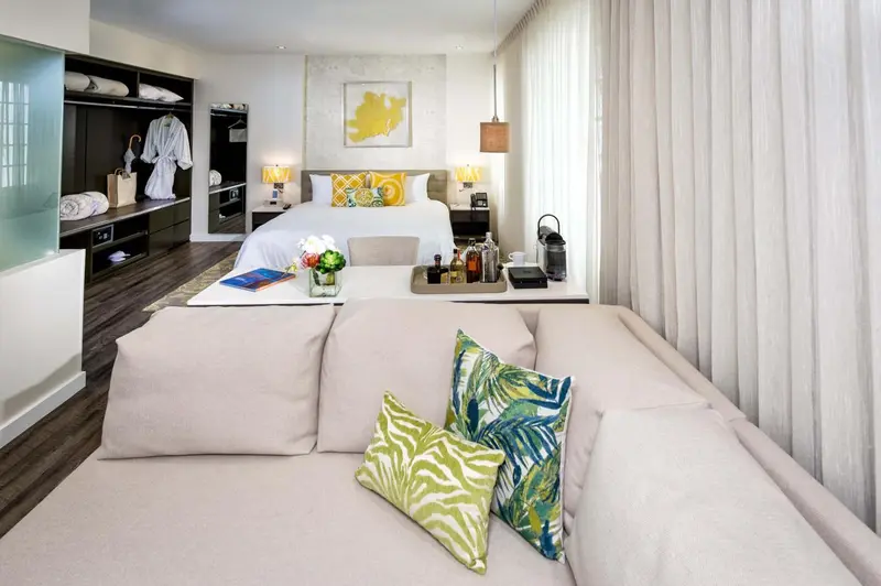 Une chambre lumineuse avec un canapé en tissu clair et un lit recouvert d'oreillers colorés.