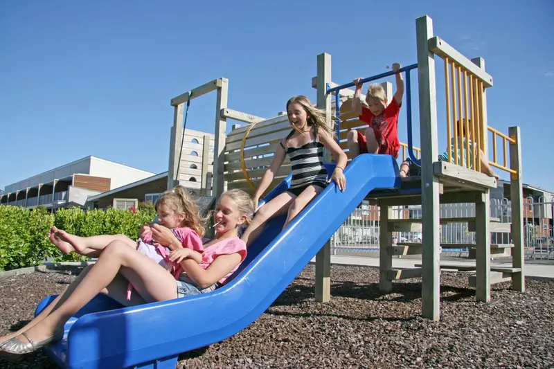 Des enfants jouent sur un toboggan bleu dans un espace de jeux extérieur.